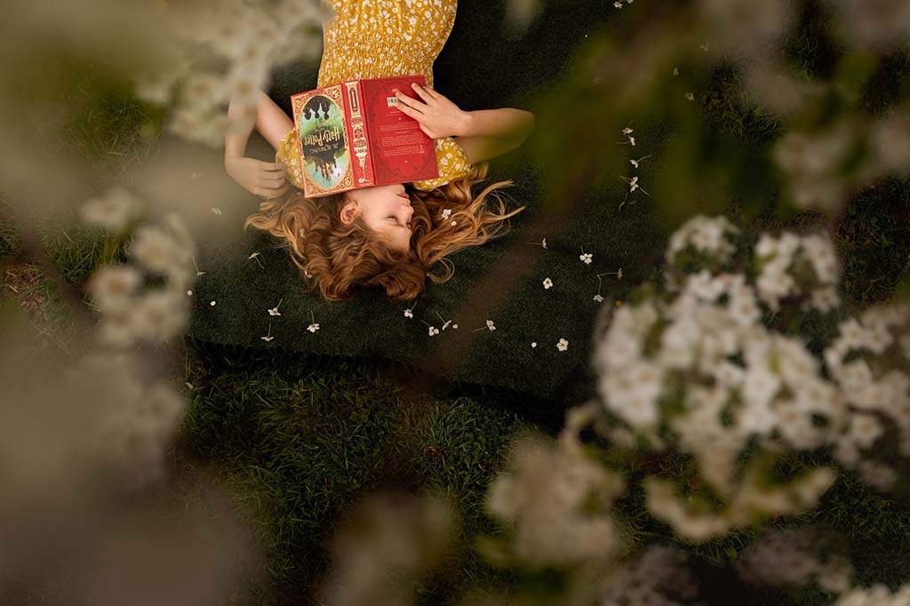 girl laying in grass with harry potter book and flowers in her hair