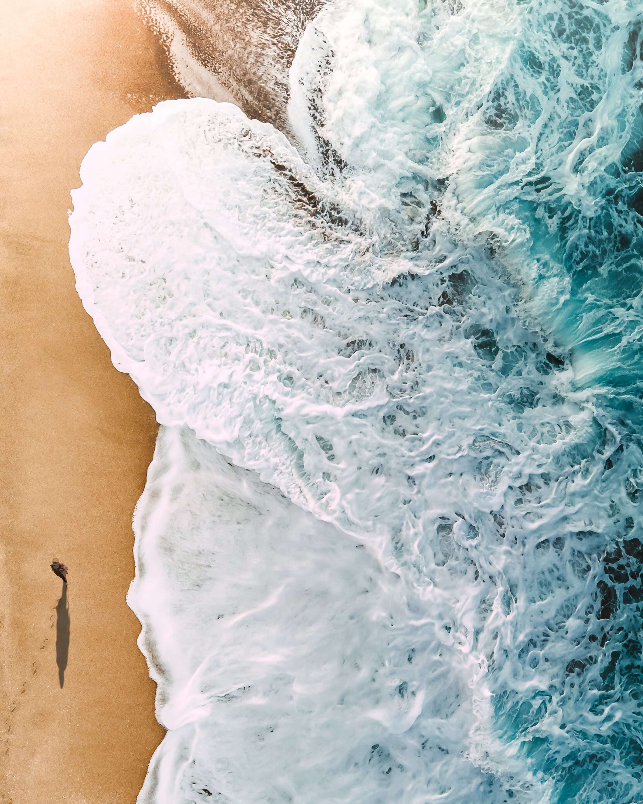 top down shot of person walking on the beach with white and blue waves